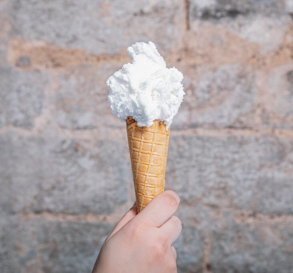 A Hand holding lemon flavored artisan ice cream. Lemon ice cream served in a waffle cone.